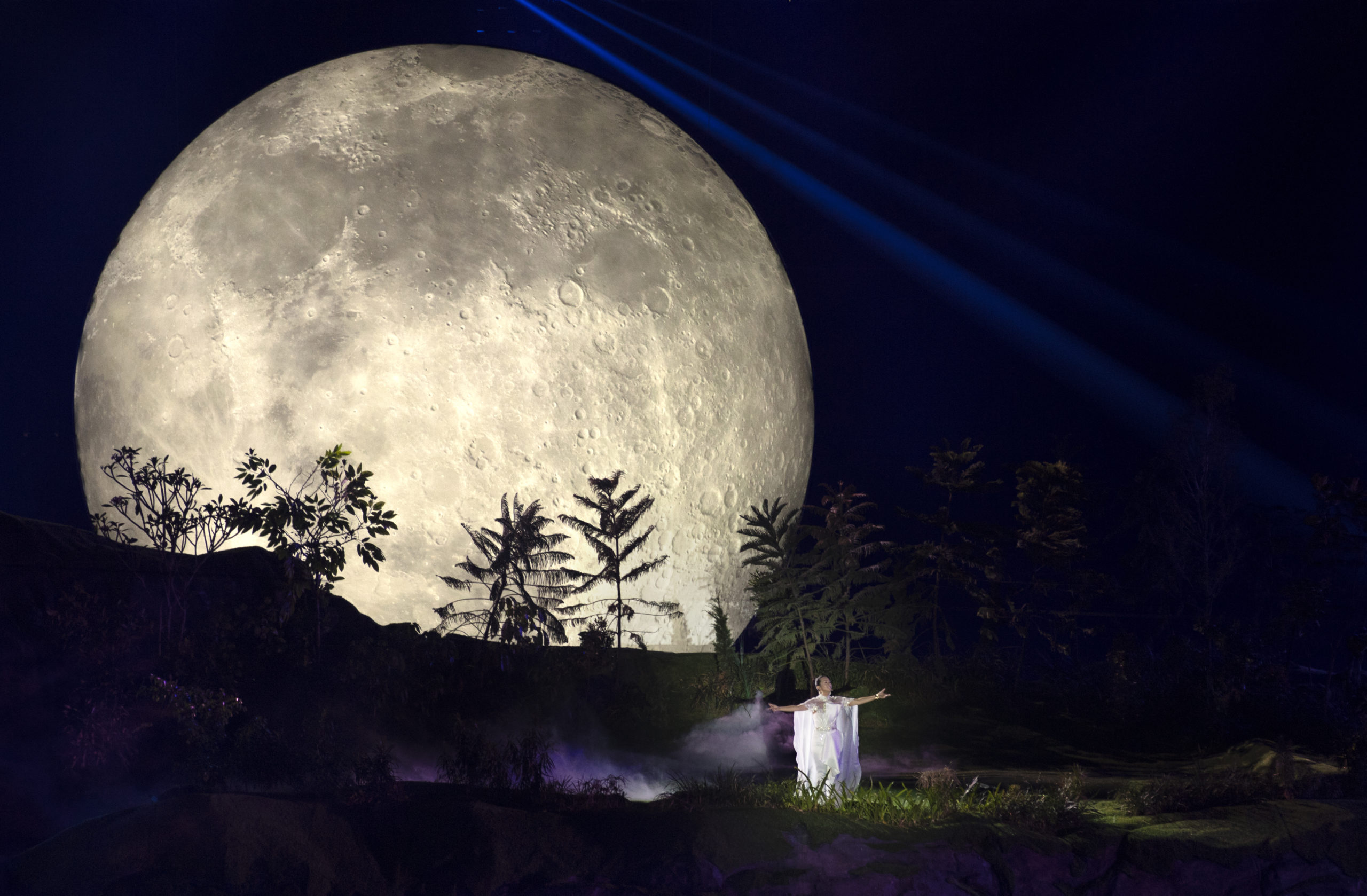 A moon rises over an actress in the backdrop of a theater performance